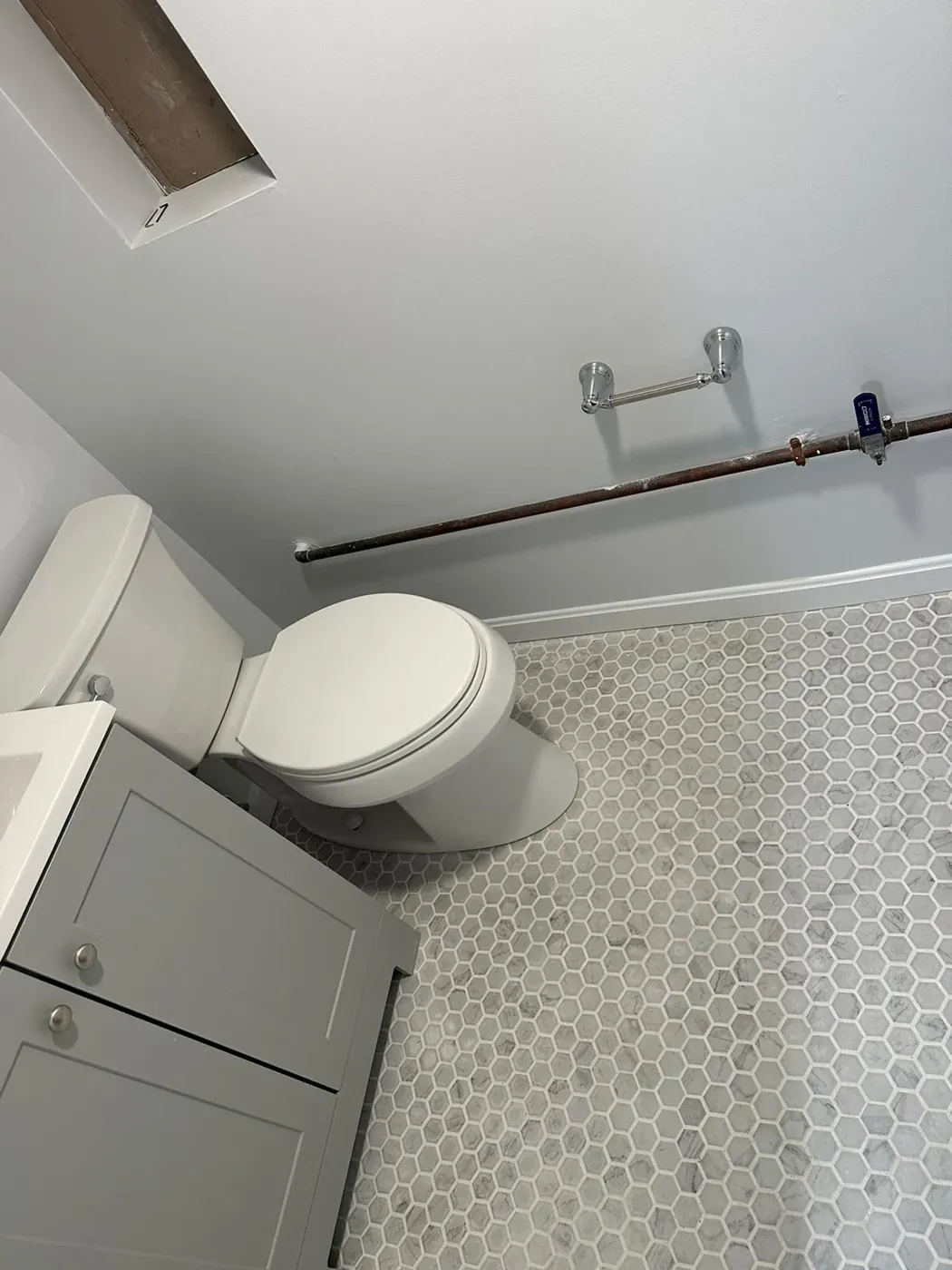 Hex mosaic tile bathroom floor fitted around a toilet base and along the baseboard