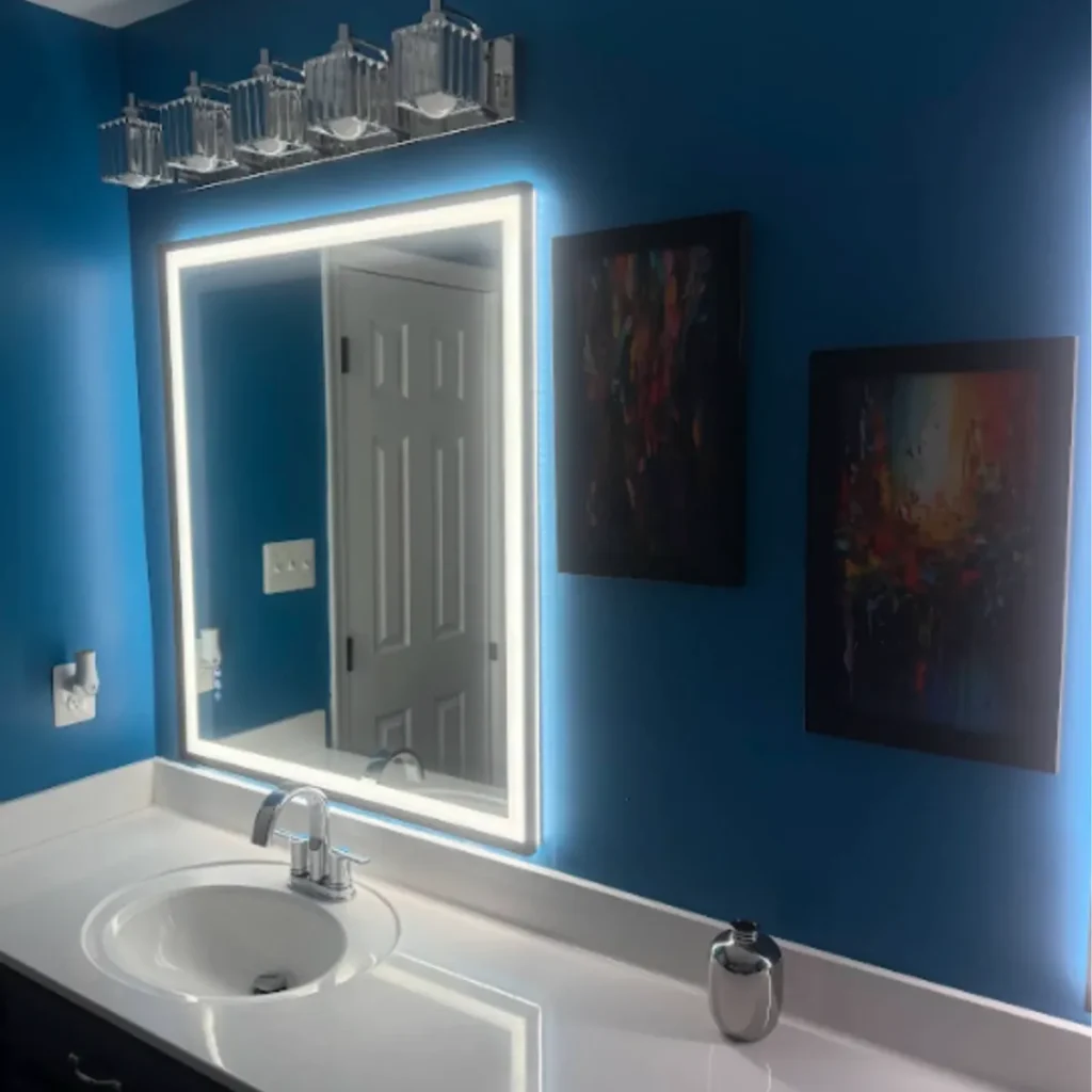 Bathroom vanity with a backlit LED mirror and a crystal light bar on a blue wall