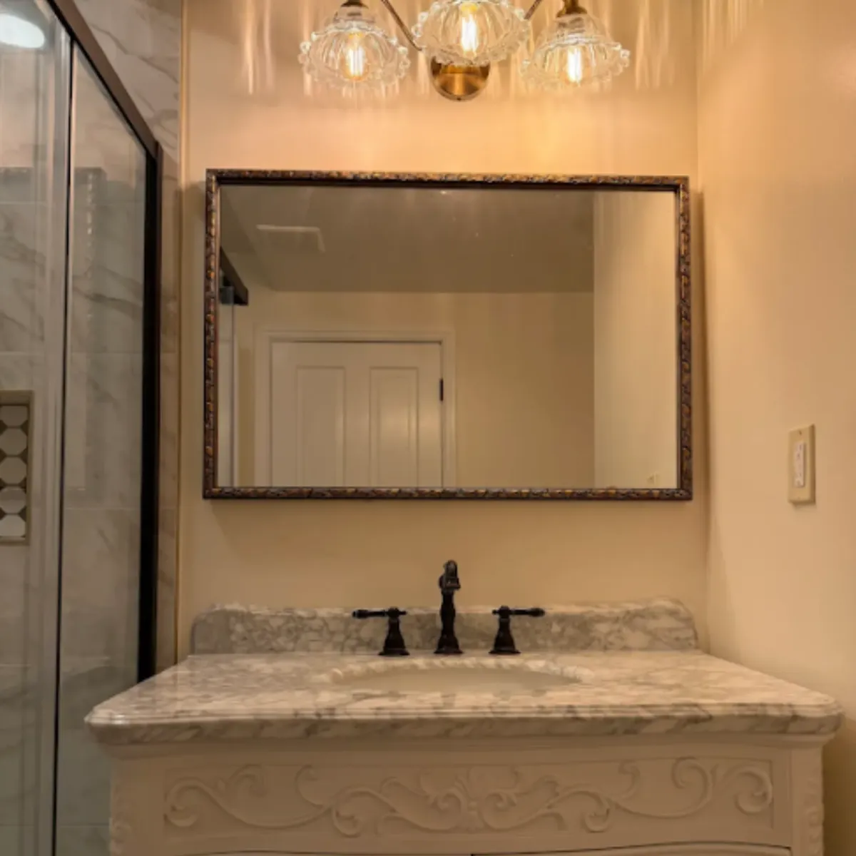 Vanity with a marble top, framed mirror and a glass chandelier overhead