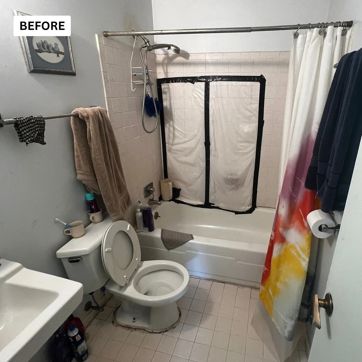 Dated bathroom before renovation with an old tub, shower curtain and cluttered storage