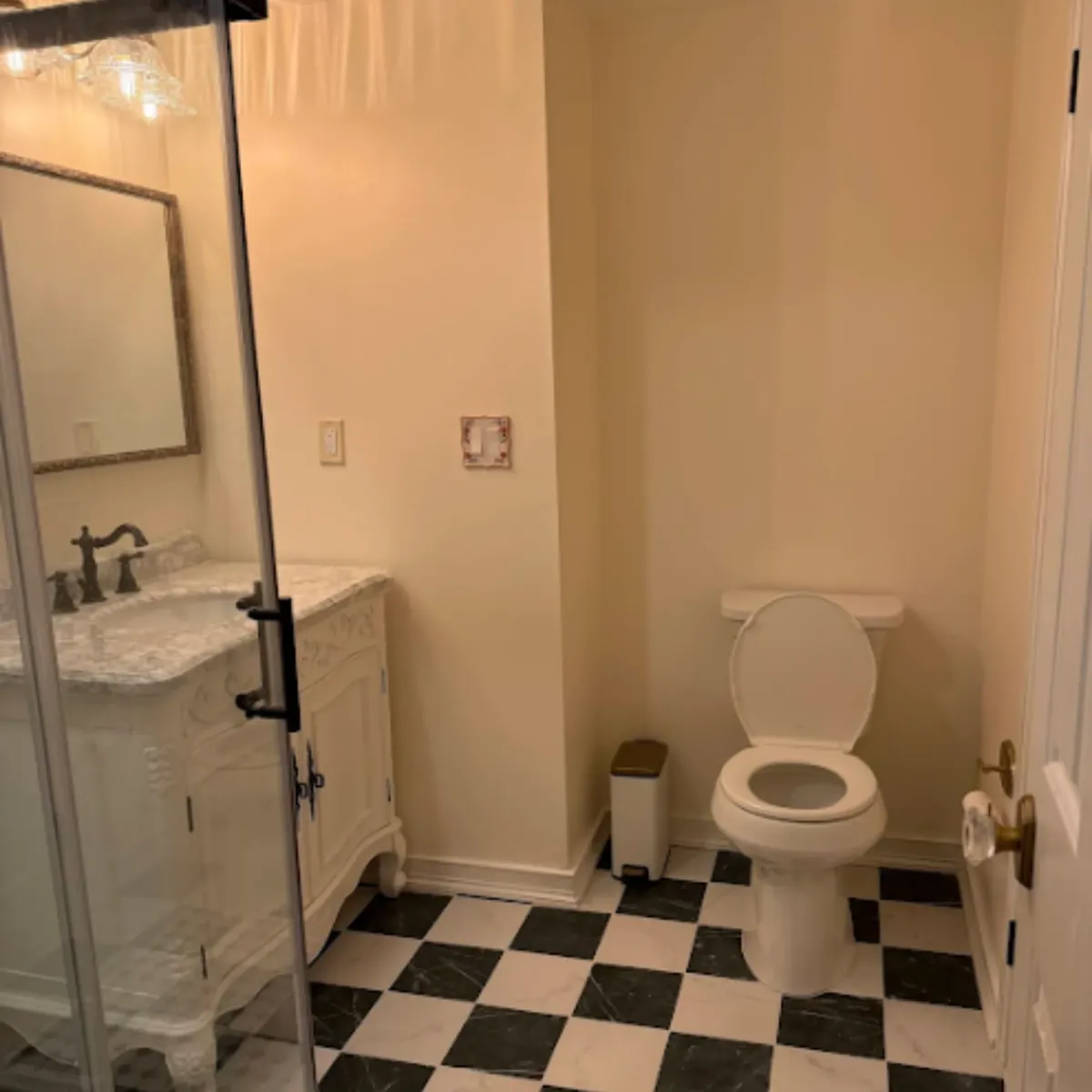 Remodeled powder room with a white toilet, marble top vanity and checkerboard floor