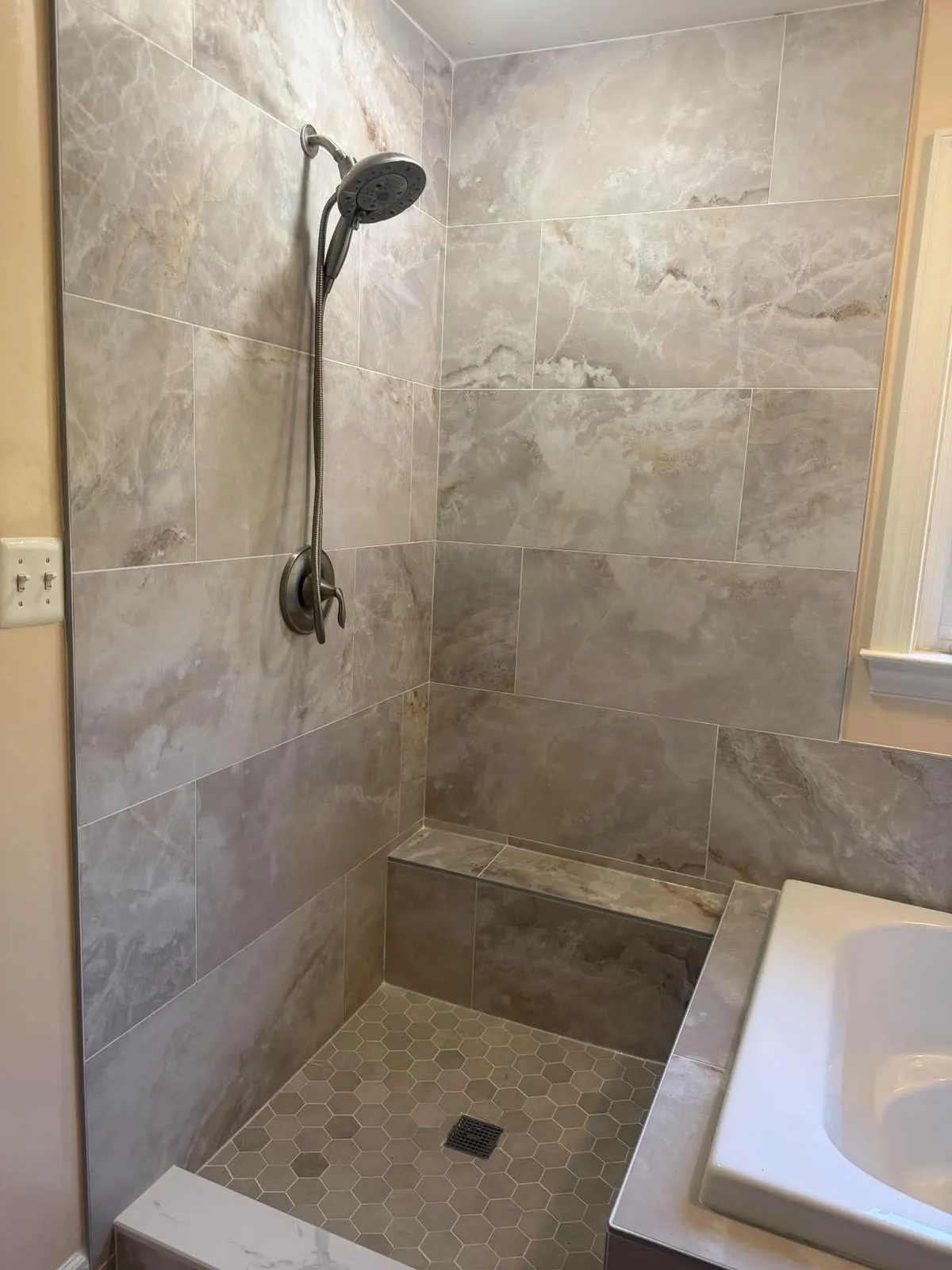 Tiled walk in shower with a built in bench, handheld sprayer and a low threshold in a Pasadena MD bathroom remodel
