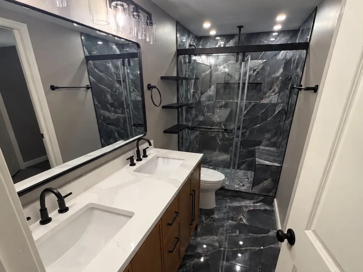 Long Pasadena MD bathroom with a double vanity, black marble floor and a glass shower at the far end