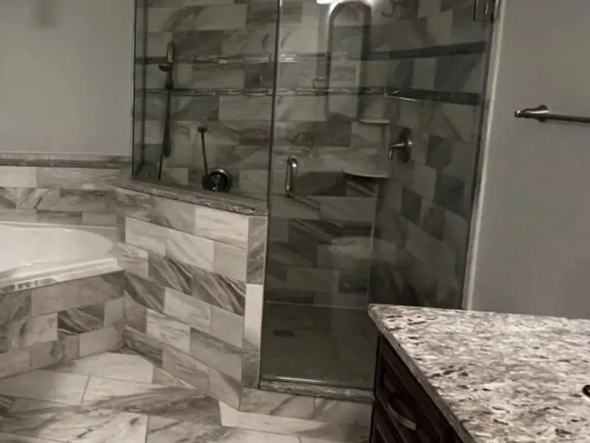 Glass panel set on a tiled curb beside a built-in tub in a Pasadena, MD bathroom