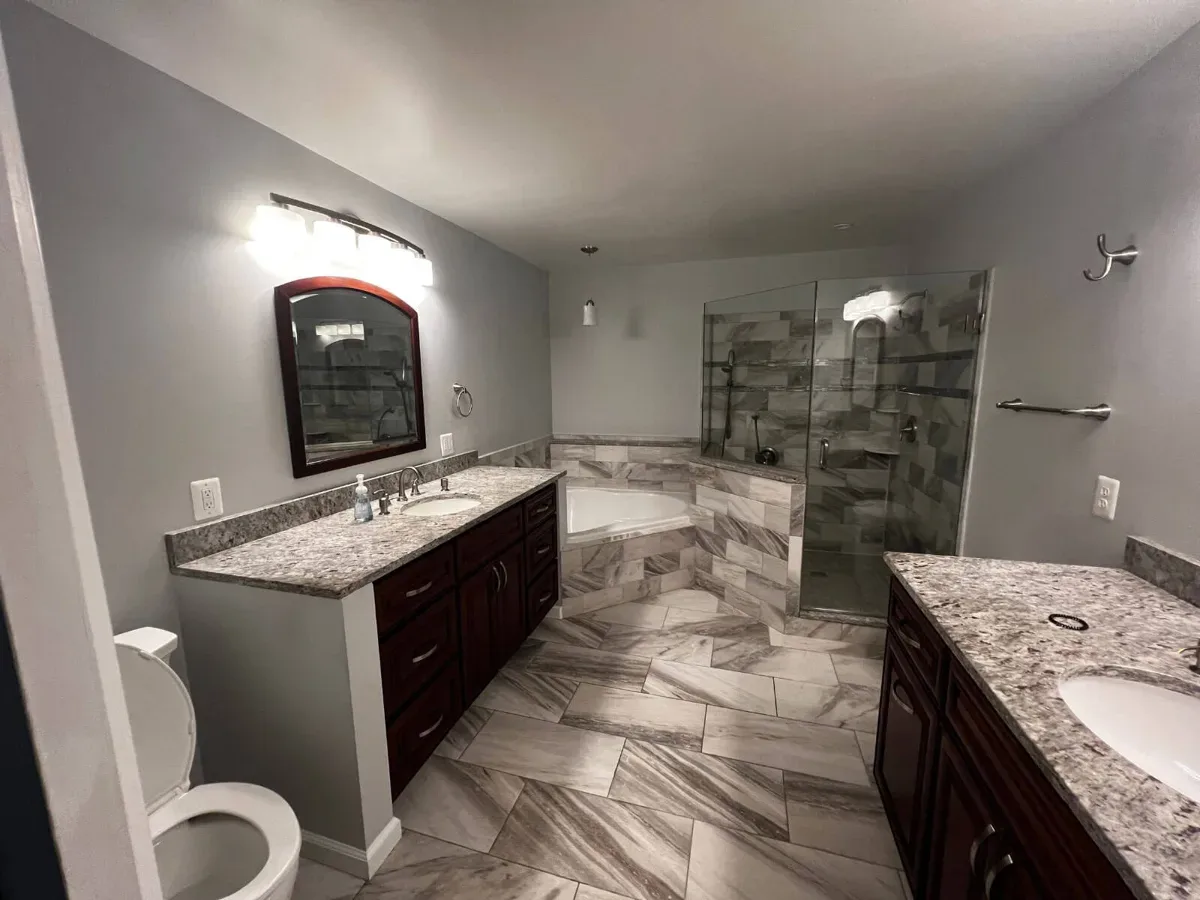 Primary bathroom in Arnold MD with two granite vanities, a corner soaking tub and a glass shower