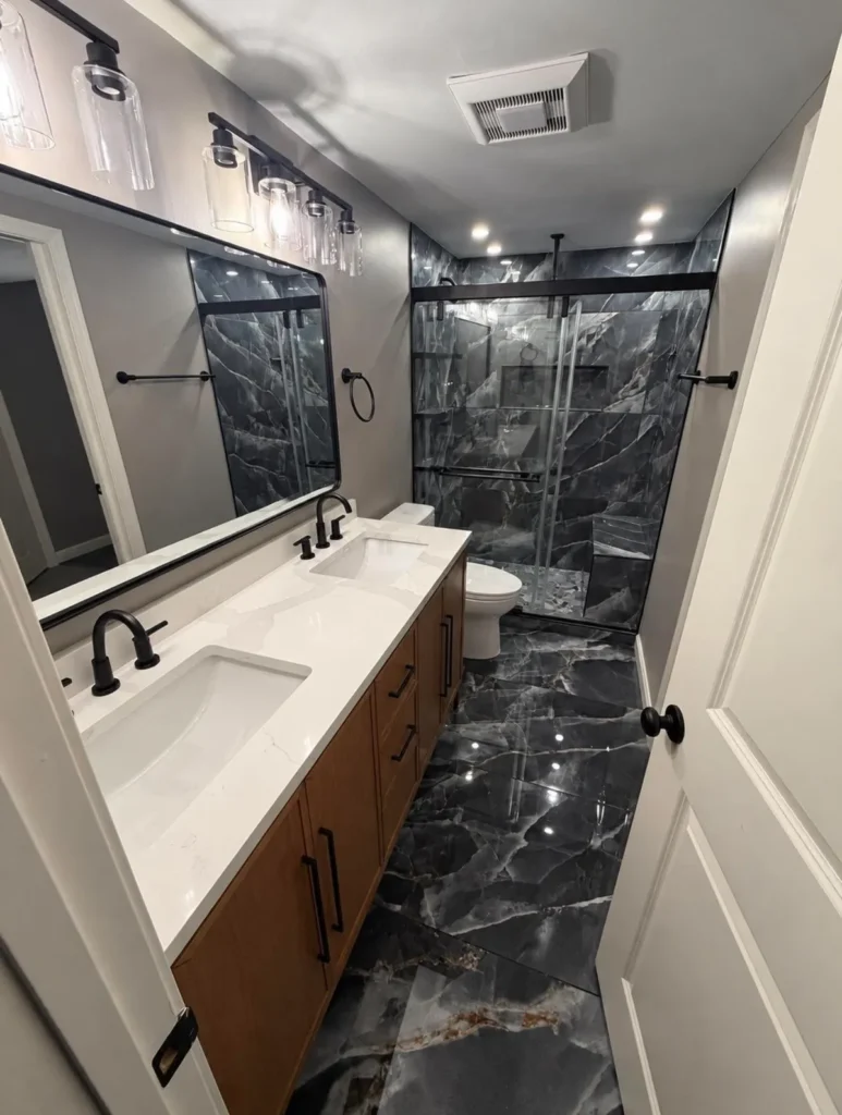 Narrow bathroom with a wall width mirror, a glass shower door and large format floor tile