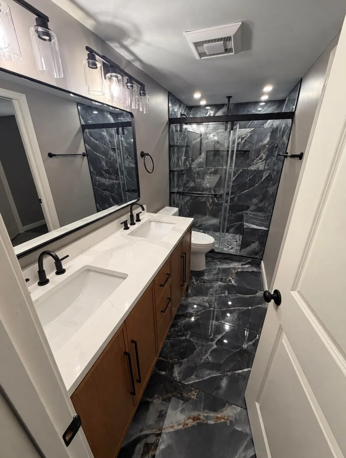 Narrow bathroom with a wall width mirror, a glass shower door and large format floor tile
